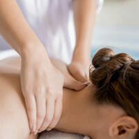 Hands of masseuse massaging neck and shoulders of relaxed client in spa salon